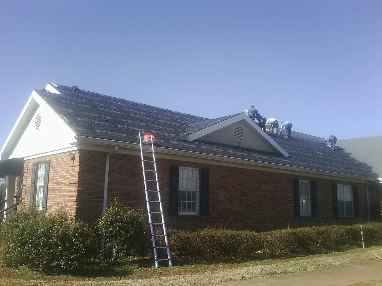 Crew tearing shingles off a brick ranch roof with a ladder set — Metal Roof Repair work by our crew in Sully