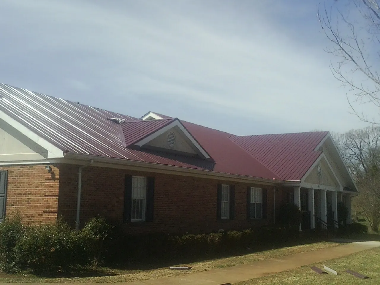 Red metal roof with gabled entries on a long brick building, from a Hail Damage Roof Repair job in Sully
