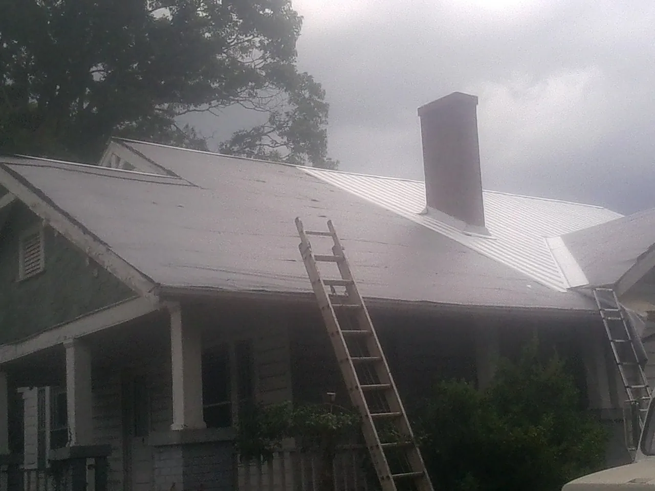 Ladders against a metal roof on an older home with a brick chimney in Sully