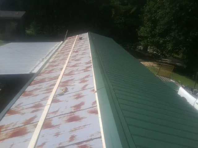 Old rusted panels beside newly installed green metal roofing — Wind Damage Roof Repair by Roofing Brothers in Sully
