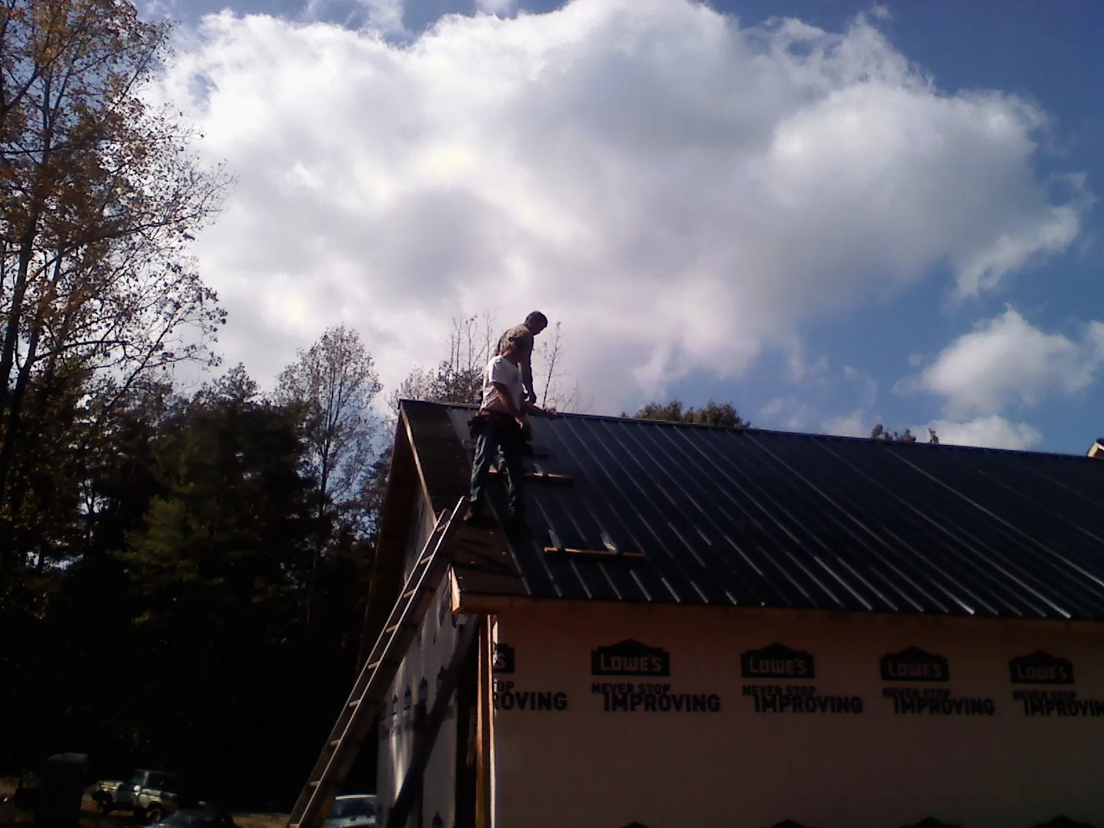 Roofer fastening dark metal panels high against a cloudy sky, from a Roof Inspection job in Sully